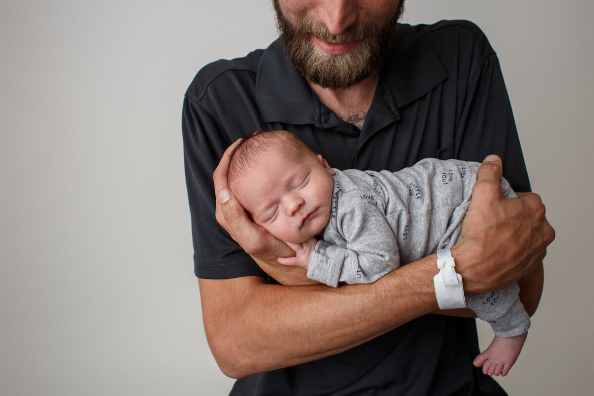 Portrait of an infant in his fathers arms photographed by professional newborn photographer