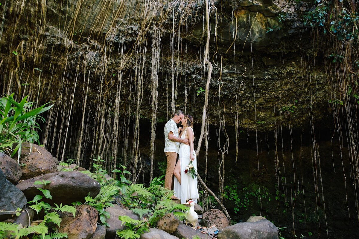 A bride and groom stand in front of large vines in Hawaii on their elopement wedding day.