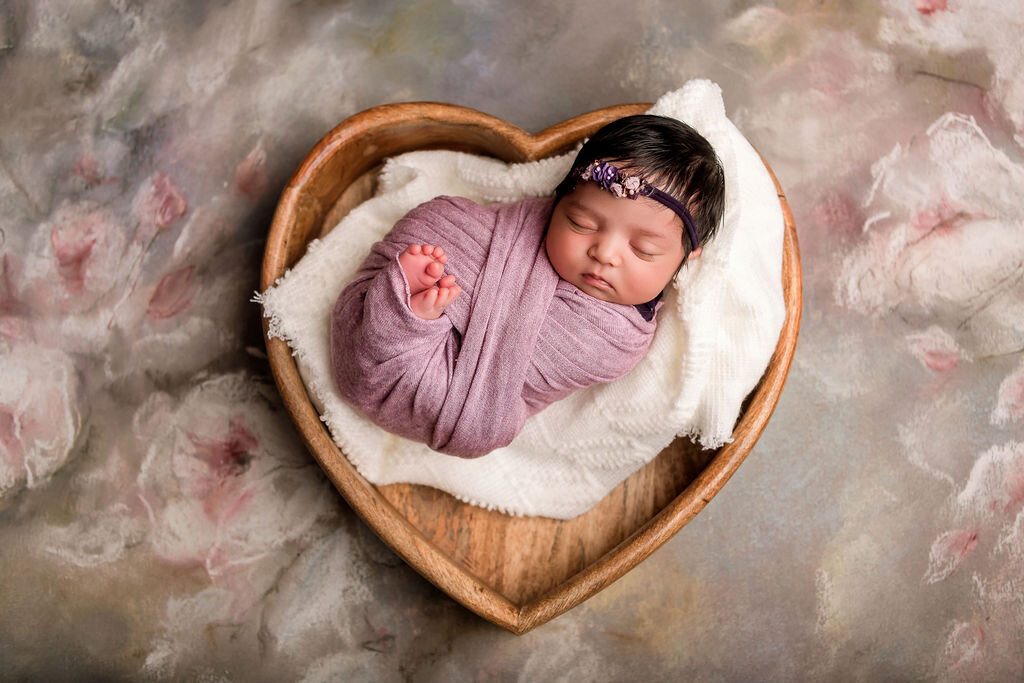 Connecticut newborn photographer creates dreamy portrait of sleeping baby in heart-shaped wooden bowl with purple wrap and floral headband