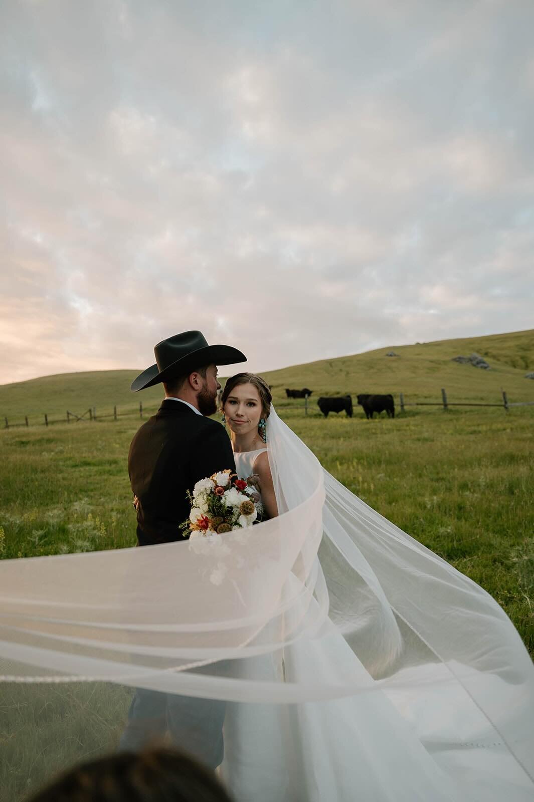 Bride and groom embracing at ranch wedding with veil sweeping in the wind.