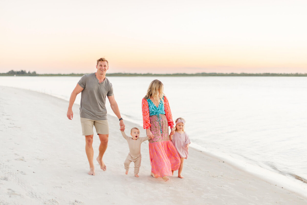 Family of four laugh and smile as they walk near the water on the beach east of Orlando