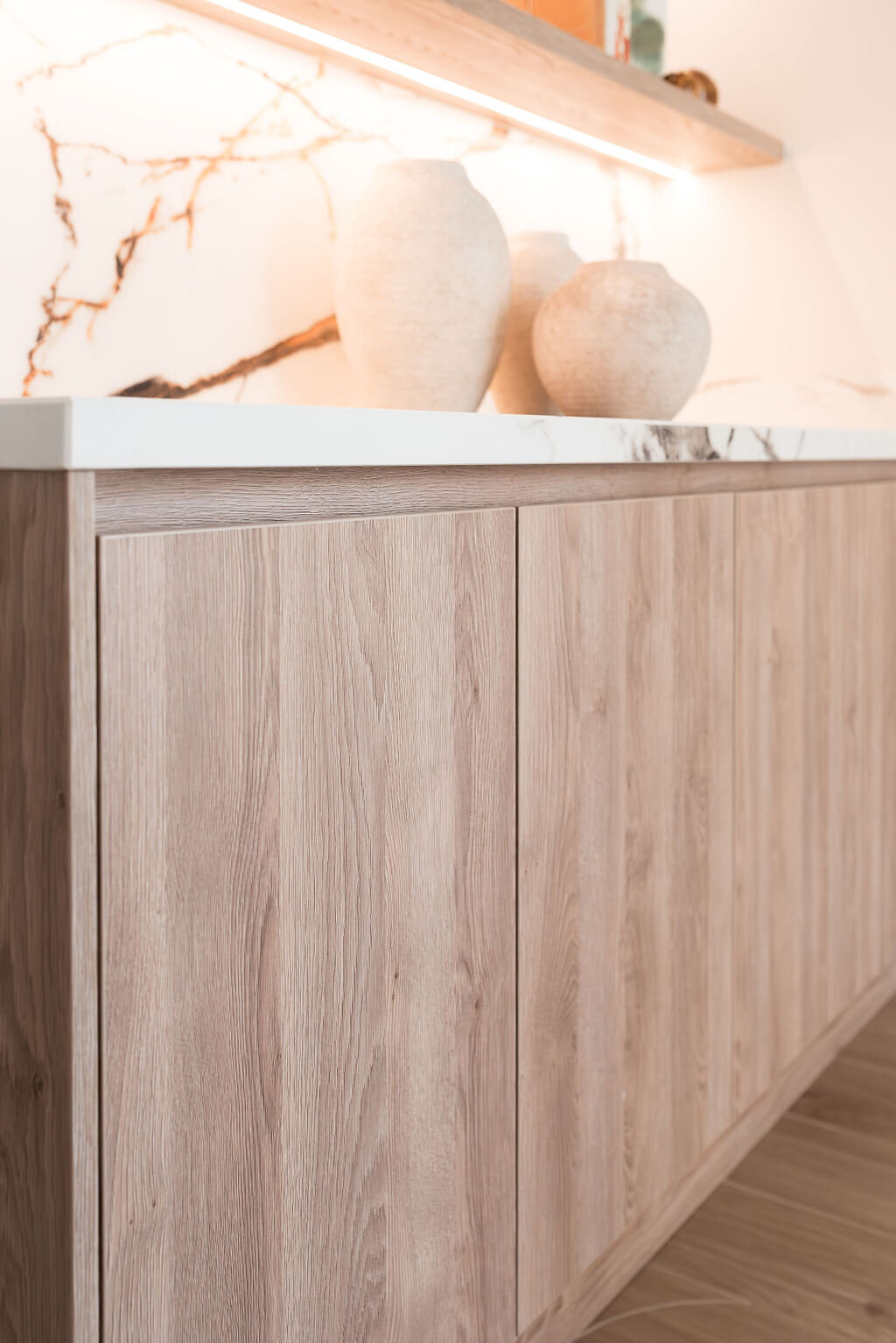 Built-in shelving bar with a light wooden cabinet at the base. The cabinet has a marble counter and backsplash.