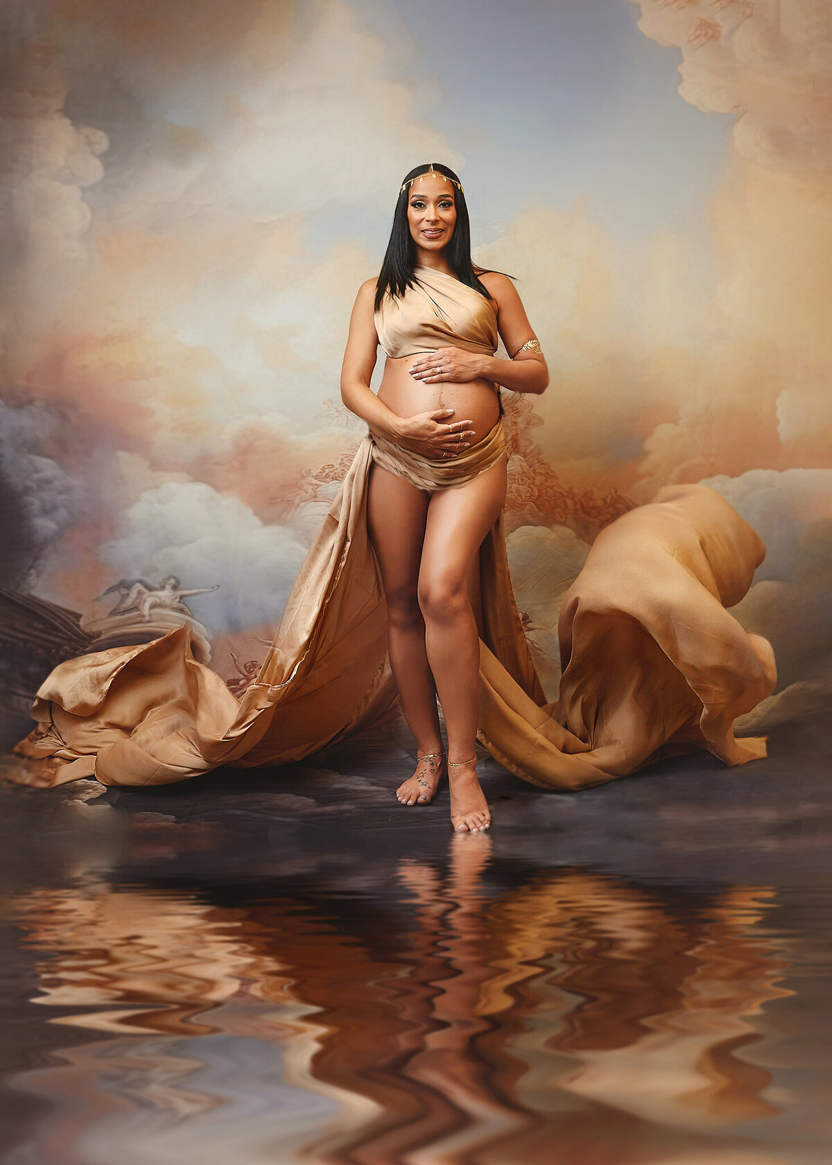 pregnant mom posing in gold silk fabric with goddess like pose and heavenly background and water reflection