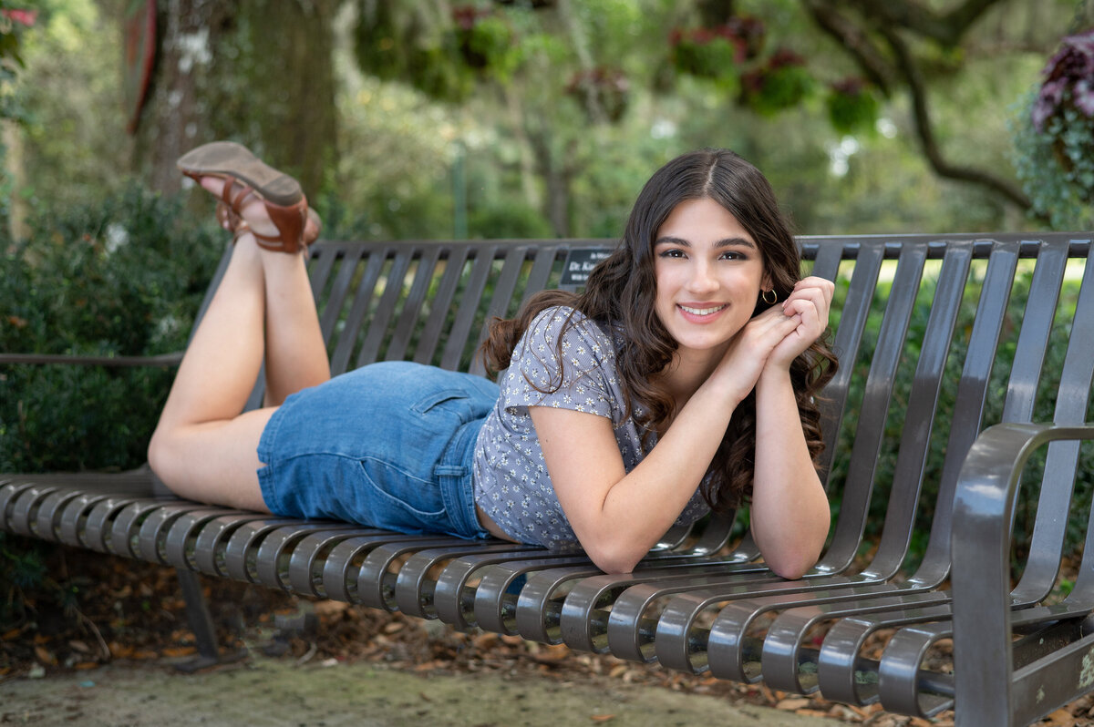 High school senior girl in casual clothes lays down on bench.