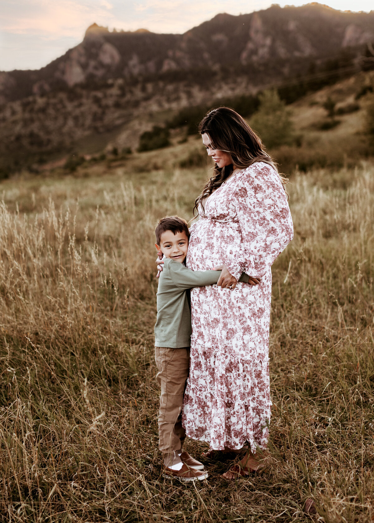 Cute expecting mother and son portrait in a field in the foothills of Colorado at sunset
