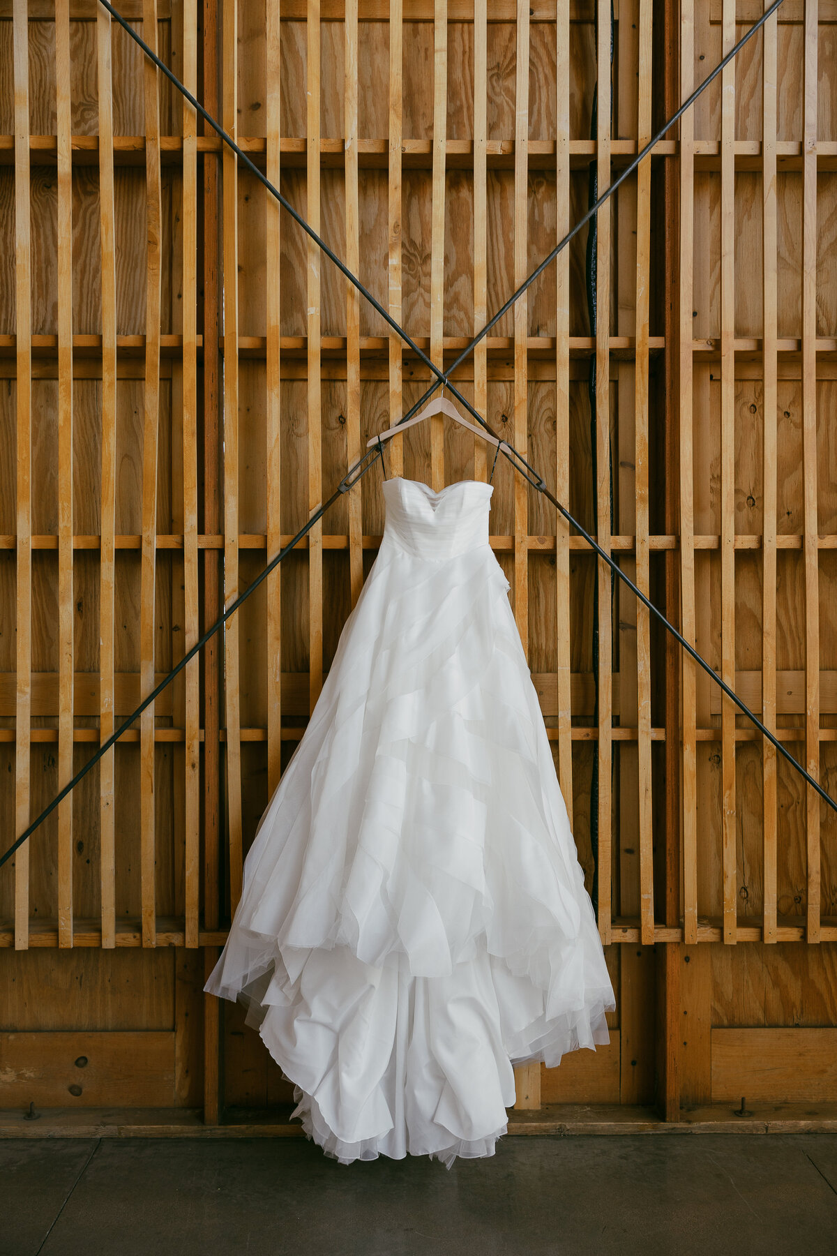 a bridal gown hangs against a wooden backdrop