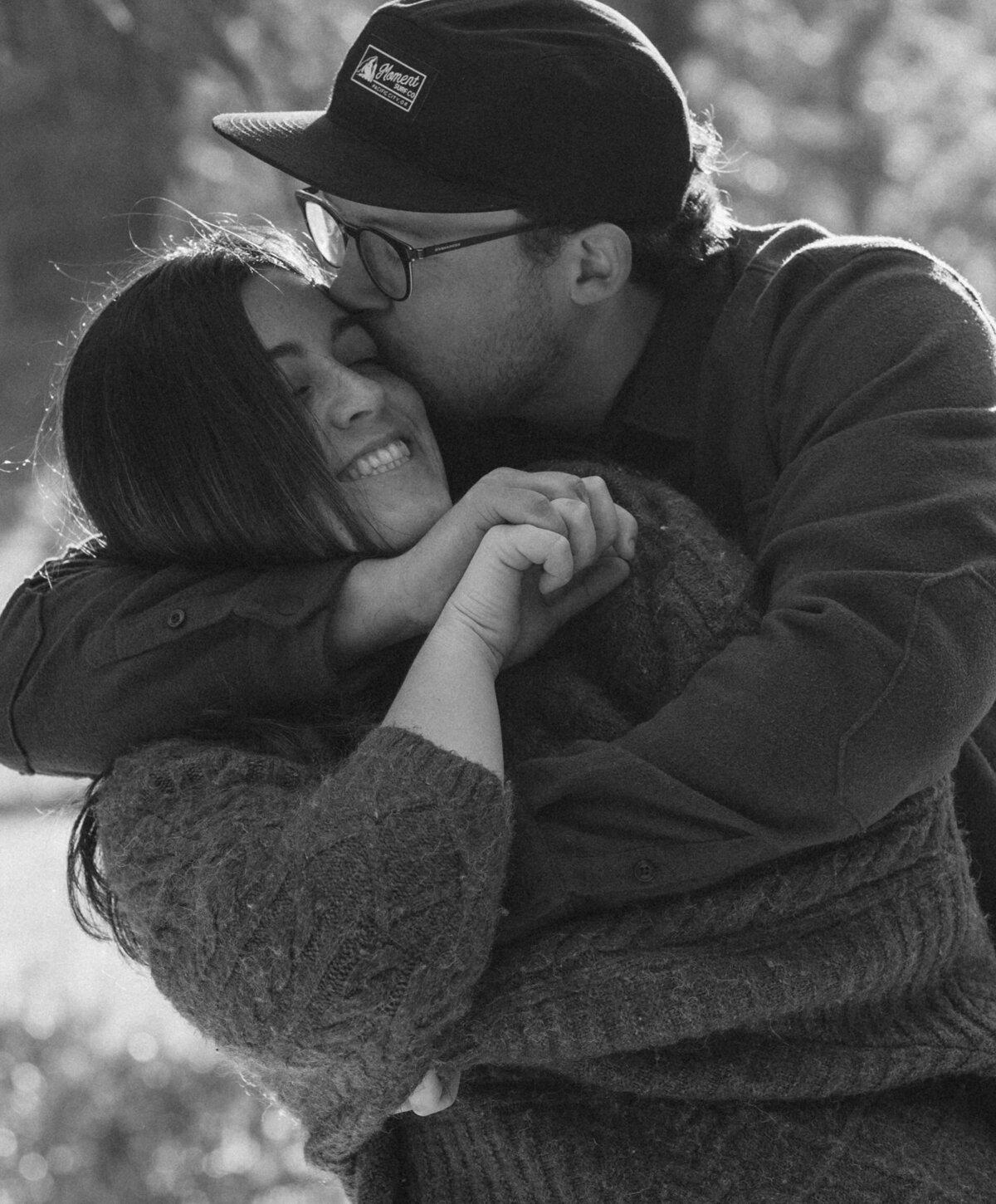 man puts his arms around his girlfriend and kisses her on the cheek during a photoshoot in the woods in Bend, Oregon