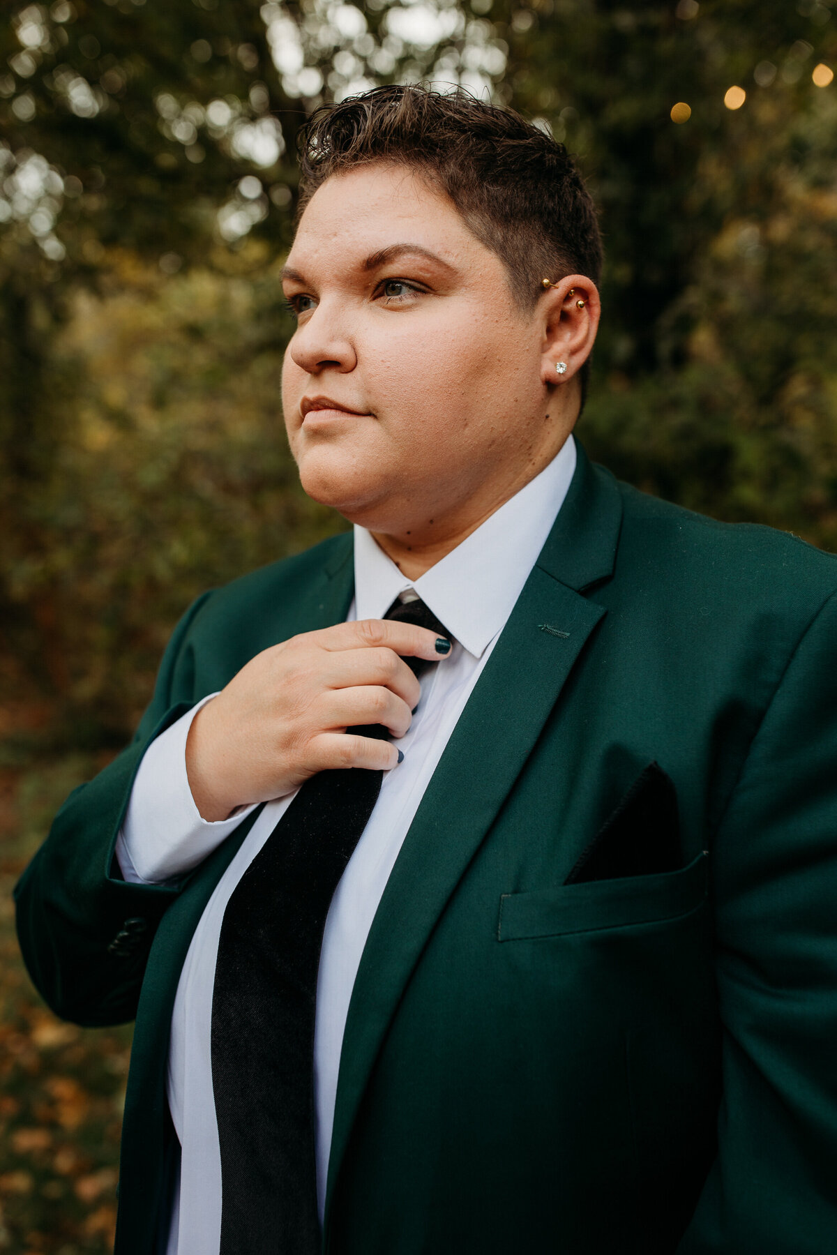 Confident individual in a green suit adjusting their tie, looking off into the distance