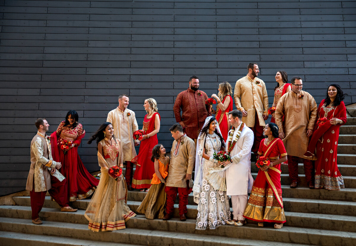 A fusion Indian wedding party group poses on steps in their native attire.