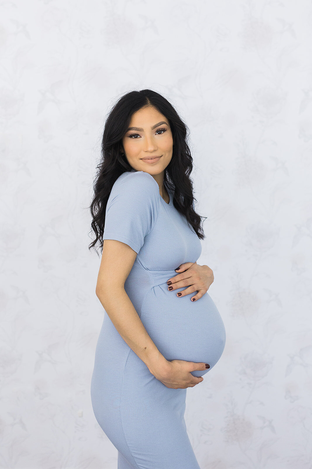 Maternity session in a studio with mom wearing a blue dress and holding her belly