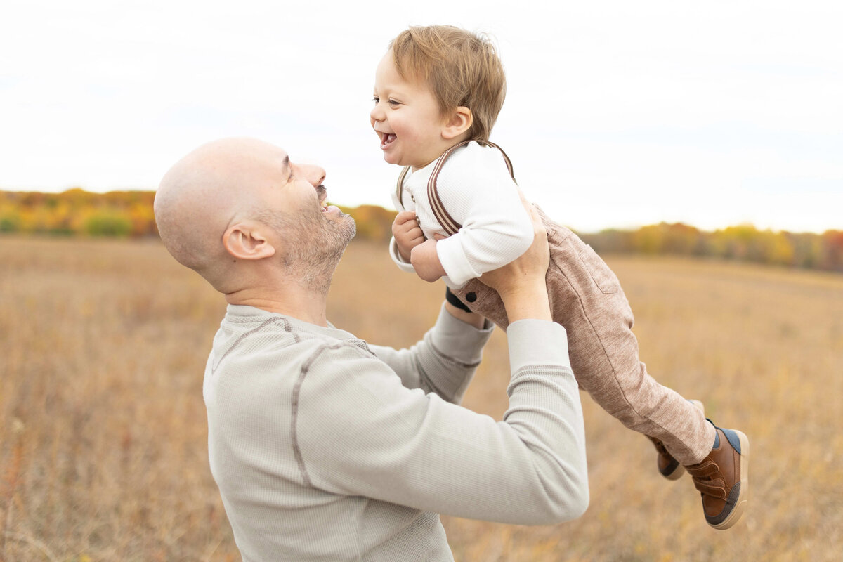 Father lifting toddler son in golden Minnesota field during family session