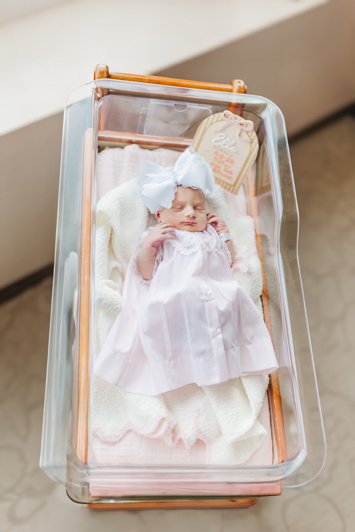 newborn baby girl in beautiful feltman brothers dress lying in hospital crib during fresh-48 session with 5u photography at grandview medical center