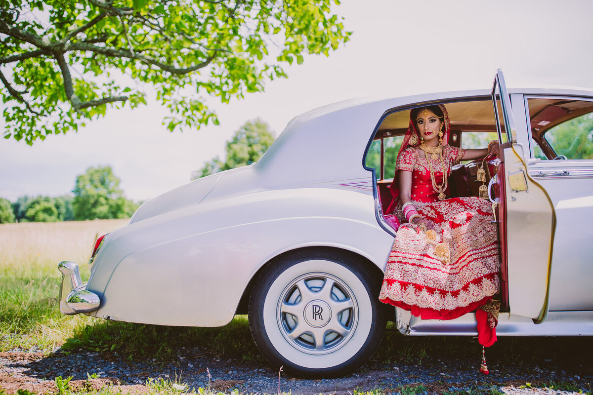 A sikh bride sitting inside the door of a vintage rolls-royce car on the wedding day