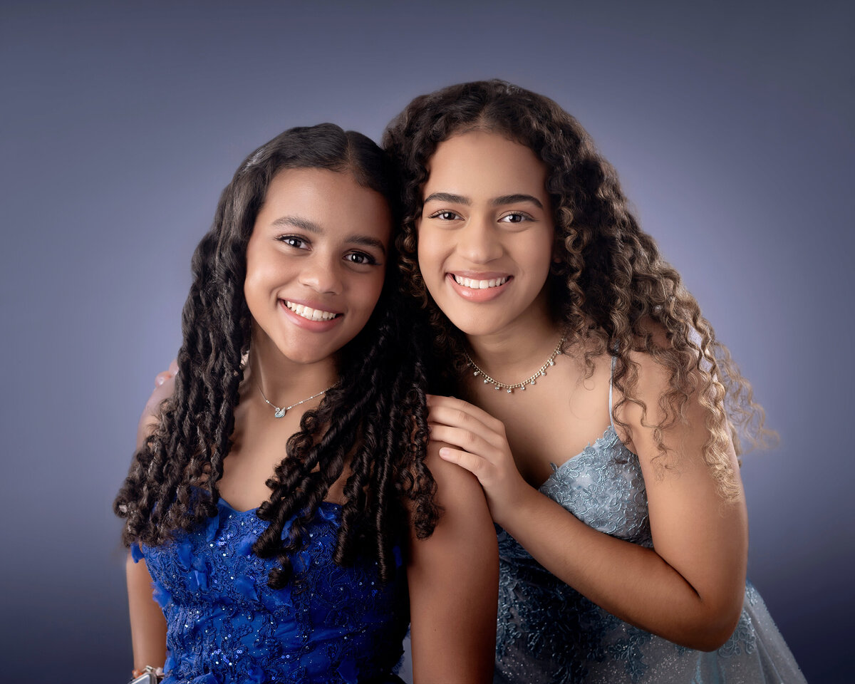 Two Sisters in elegant blue dresses against a blue background.