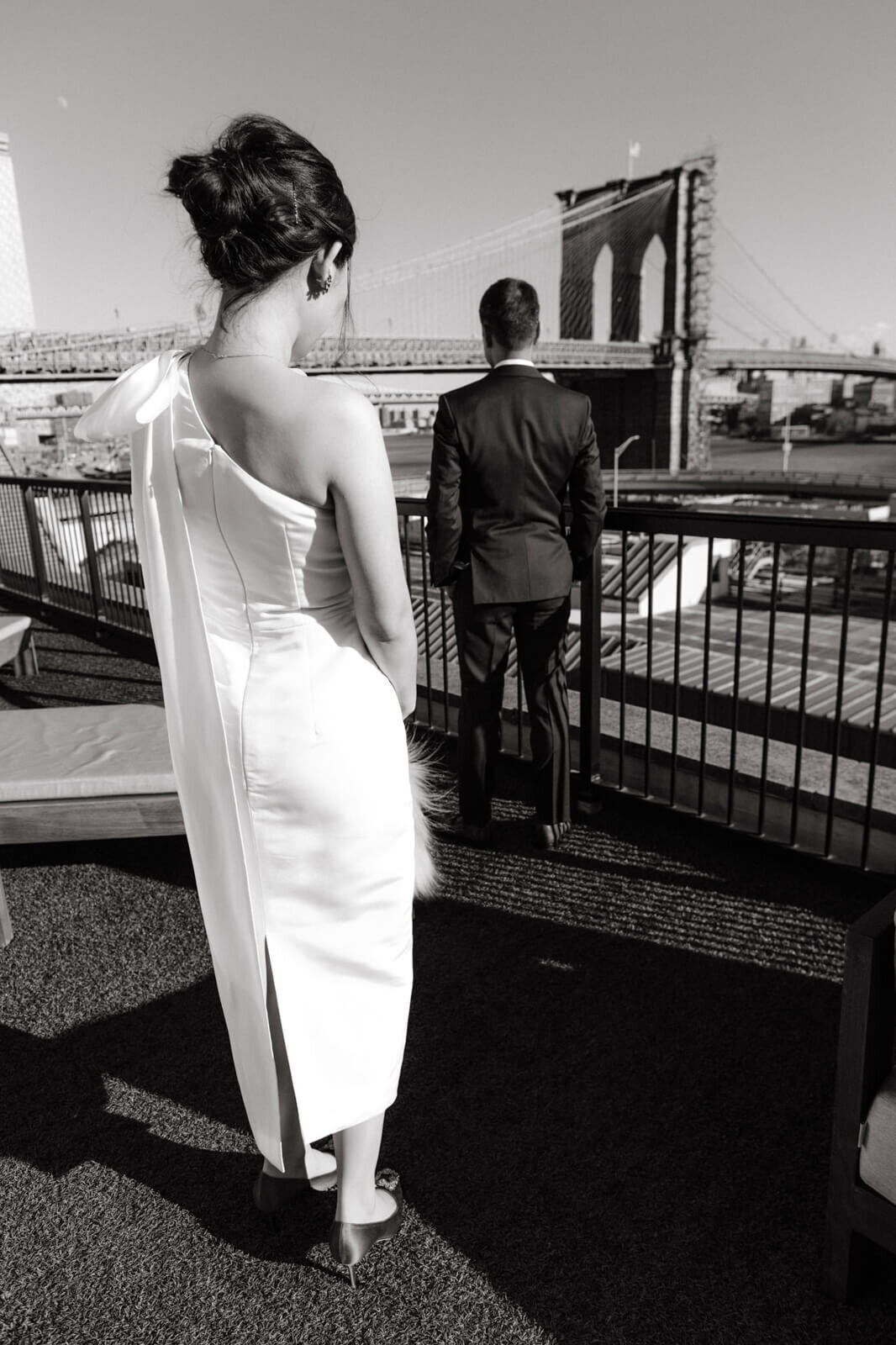 The bride and groom are on their backs, on a terrace, looking towards Brooklyn bridge.