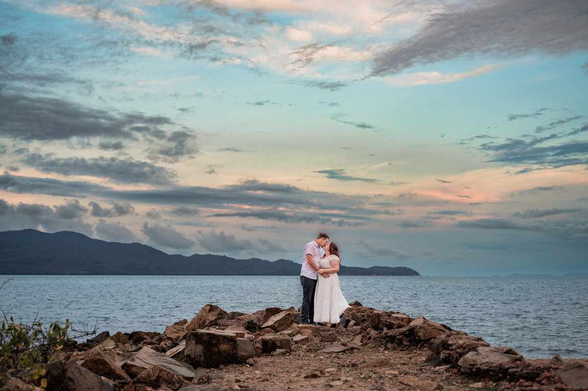 man and woman embracing on a rockwall on a townsville beach at sunset - Townsville Engagement Photography by Jamie Simmons
