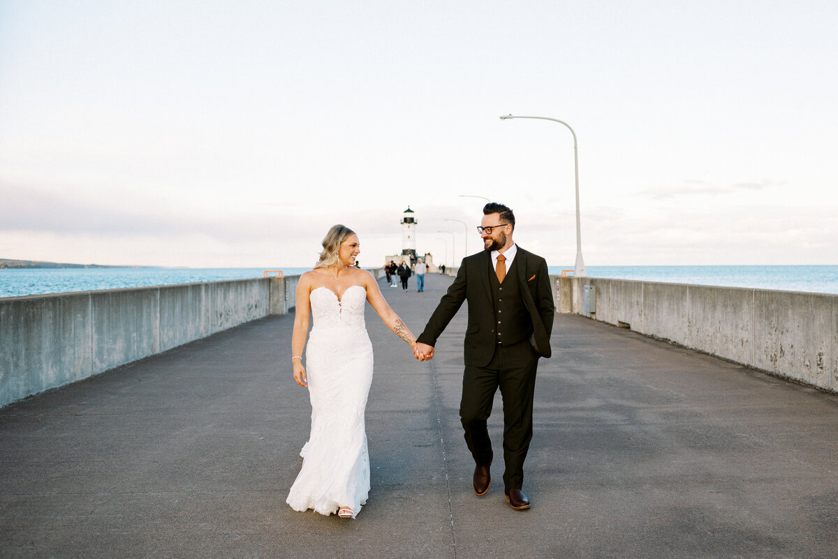 Bride and groom walking by the light house holding hands in Duluth, MN by Lake Superior