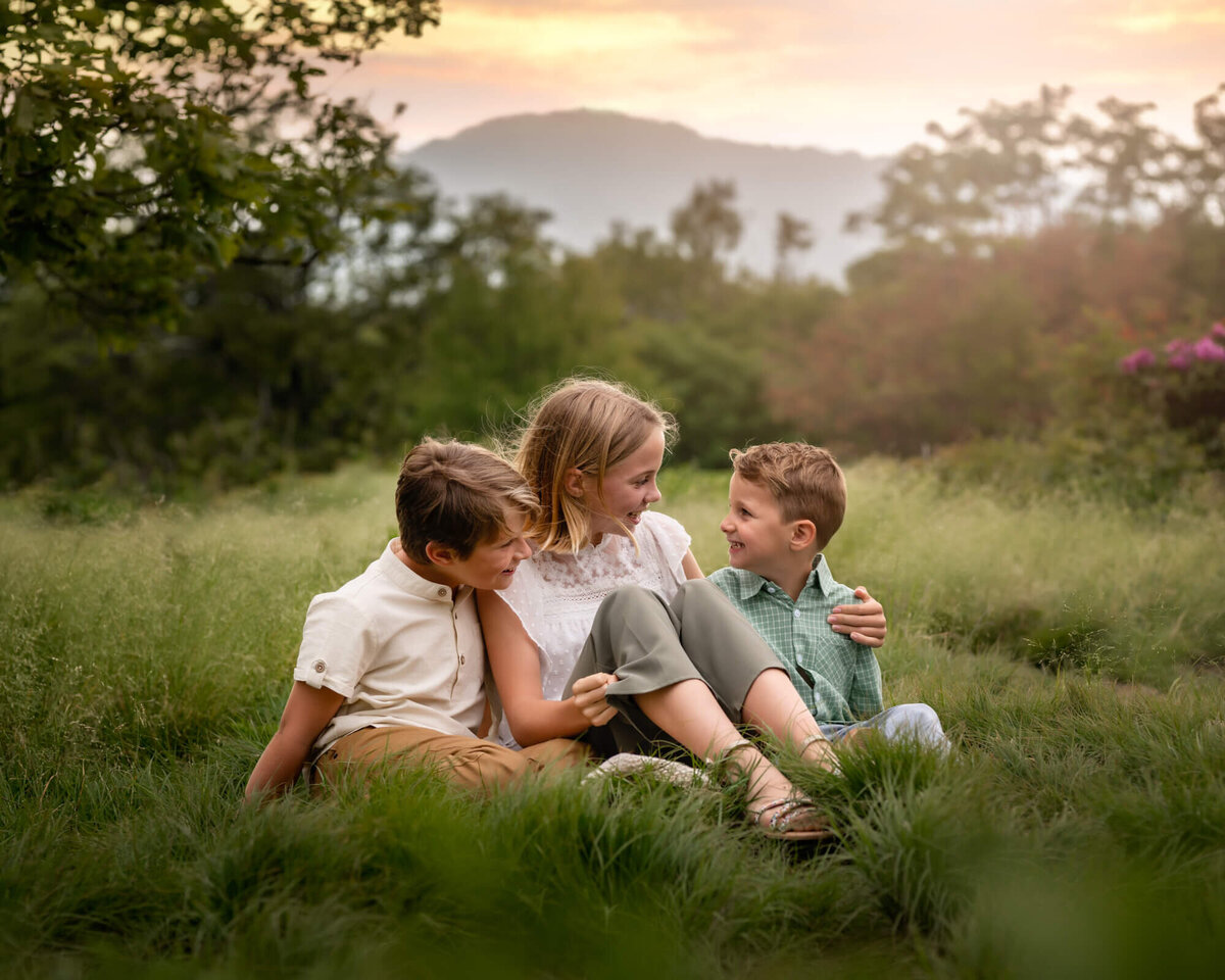 A group of three siblings sit in the grass and chat at Craggy Gardens