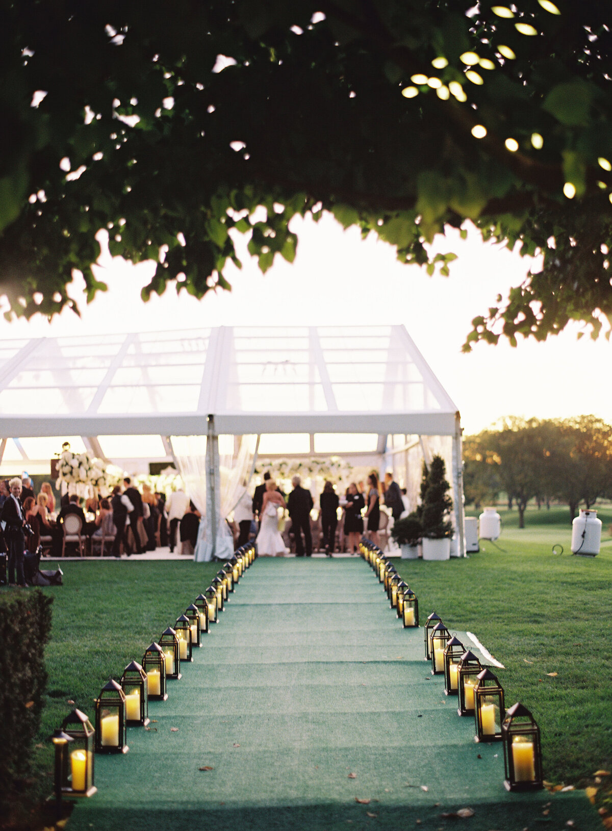 A blurred picture of the wedding tent full of people with a walkway lit with candles. 