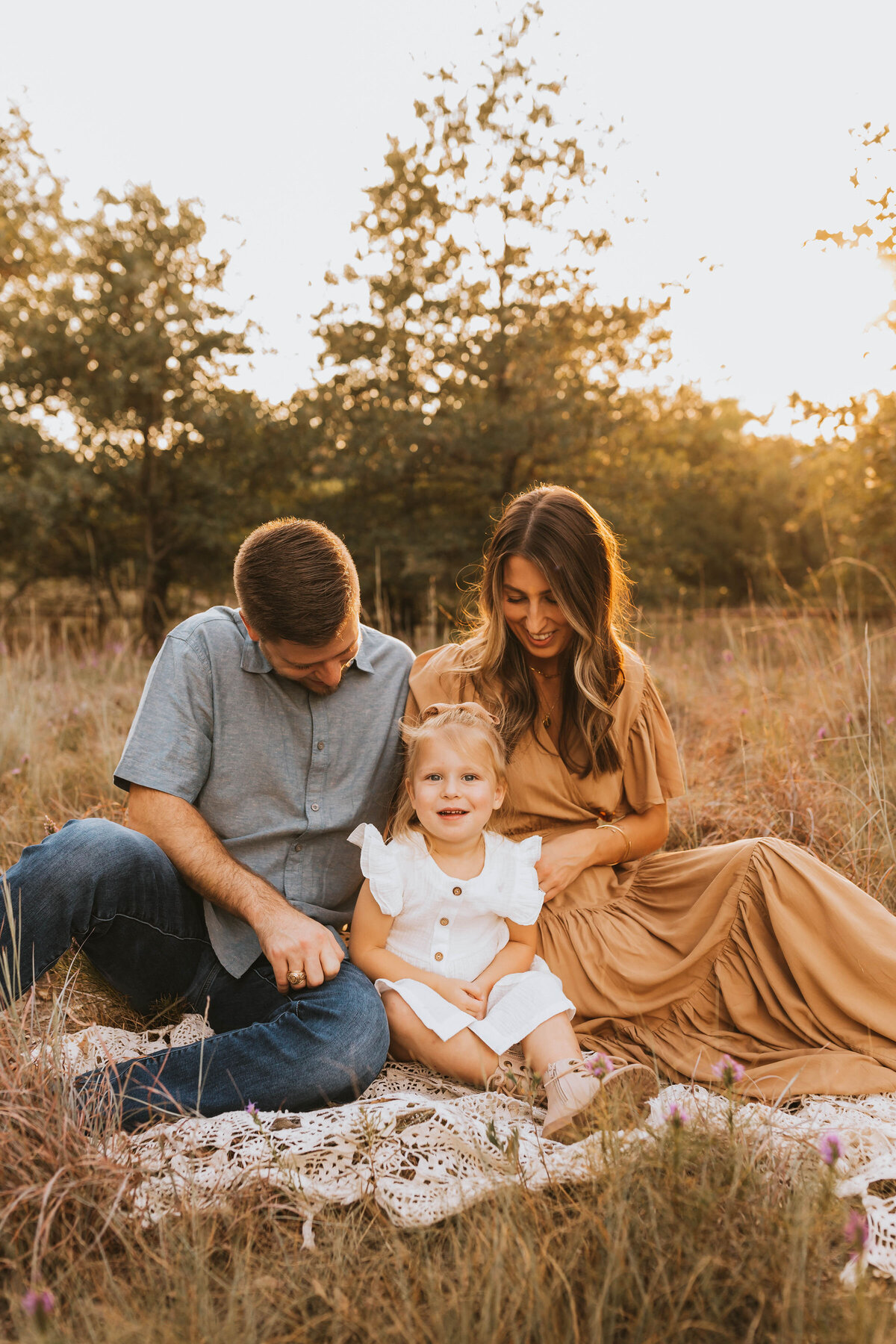 Family of three in complimentary outfits sitting on a blanket in a sunny field