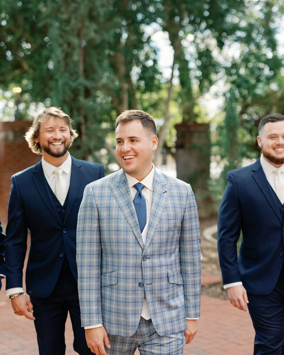 A man in a plaid suit showing how men’s dress clothing should be cared for and worn next to his two friends wearing navy suits