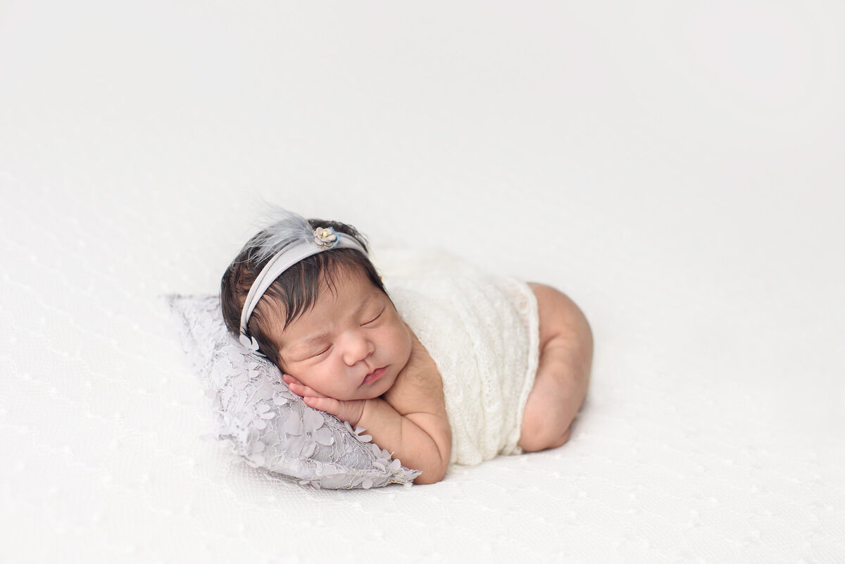 in studio photo shoot of newborn baby with a all white backdrop wrapped in blanket with head on pillow
