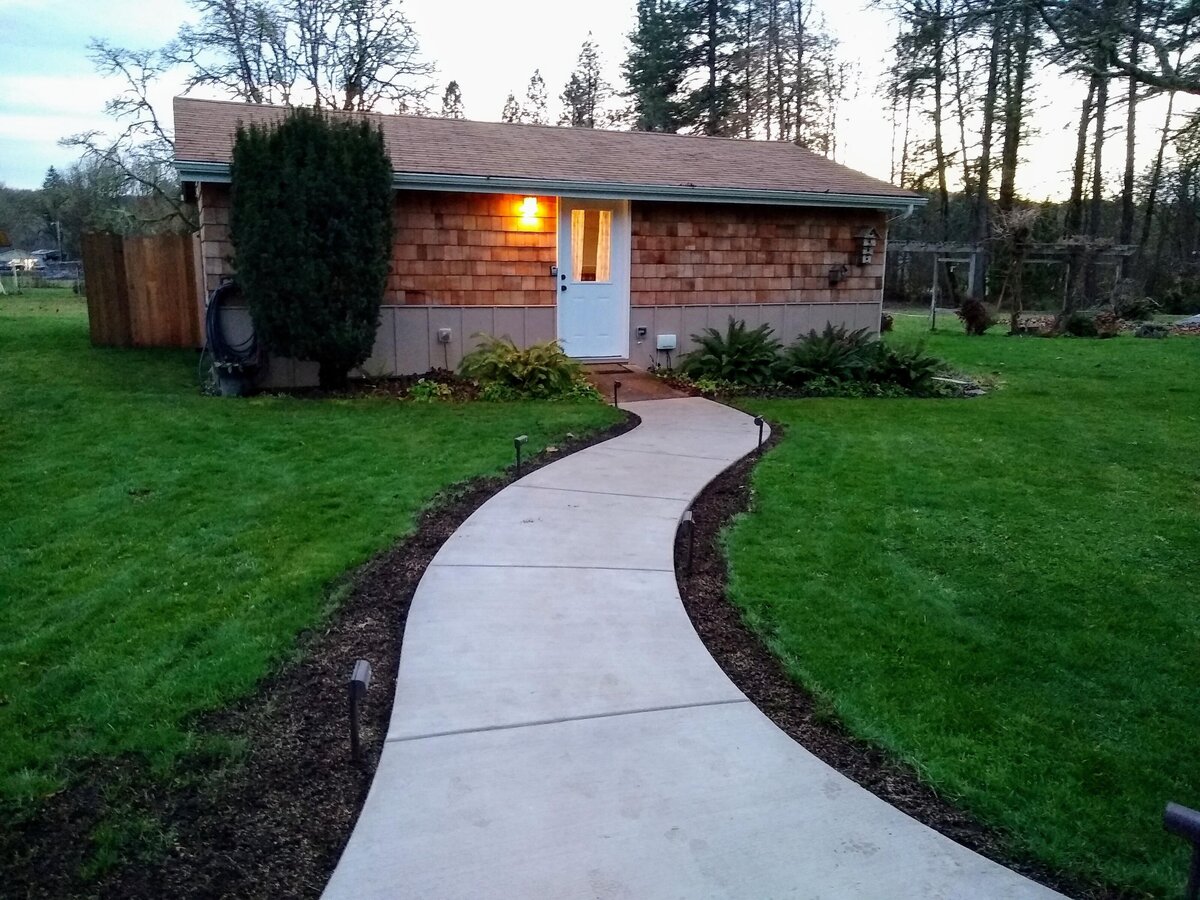 Paved entrance leads to cottage with porch light on.