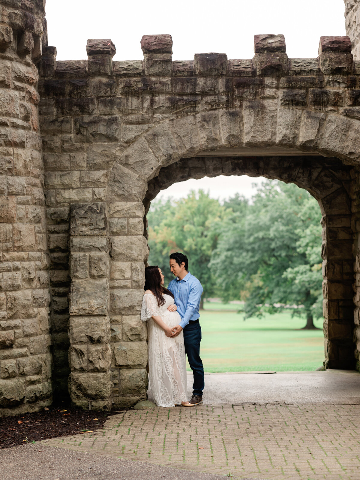 husband and pregnant mother in white lace gown holding belly for maternity portraits 