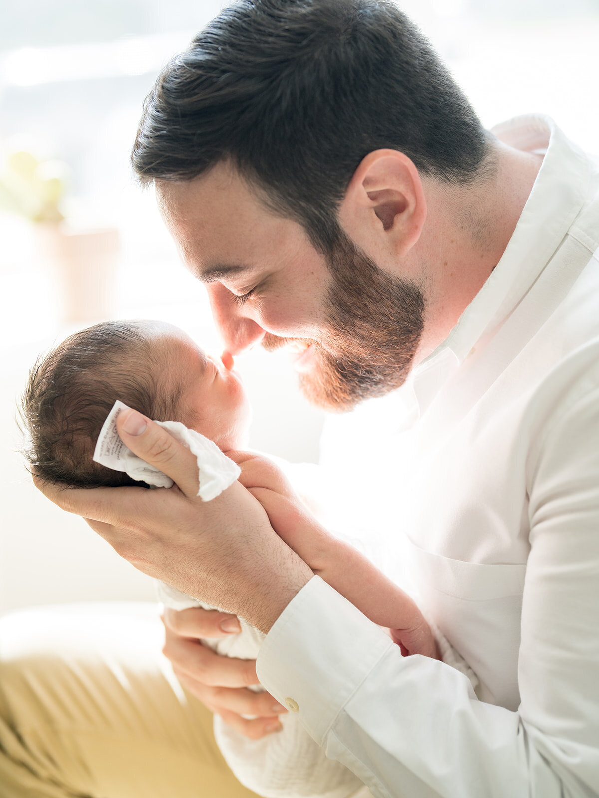 Father holds baby boy up to his nose as the sun light fills in around him.