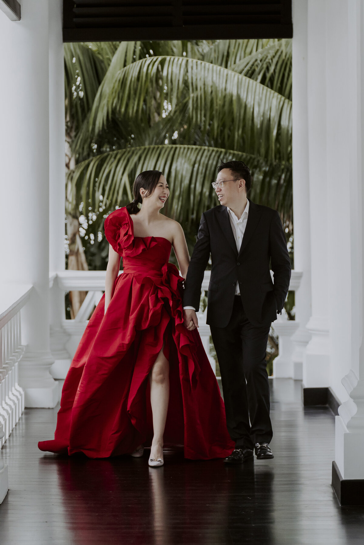 The bride in her red cheongsam dress and the groom in his black suit walking in the raffles hotel