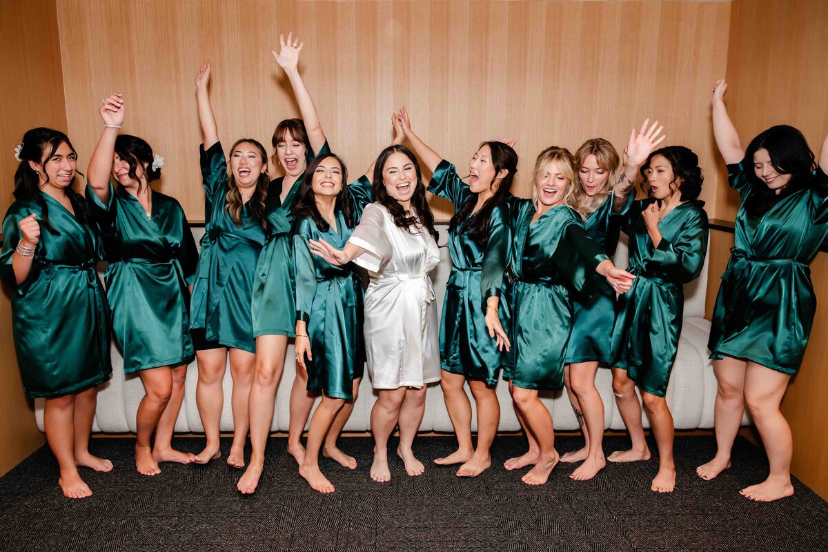 Bridesmaids wearing teal robes celebrate with bride