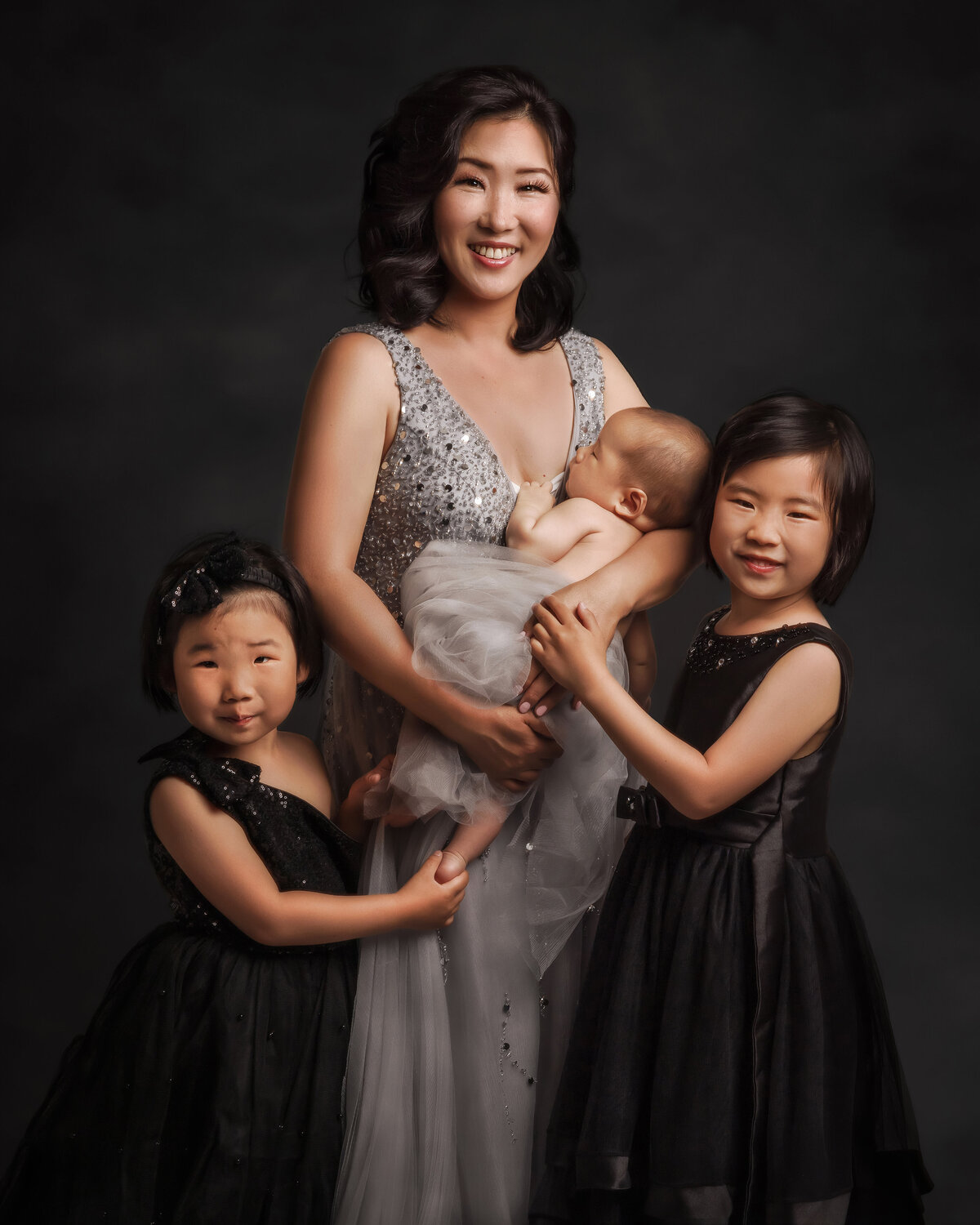 mom in a silver dress and girls wearing black on grey backdrop near dupont