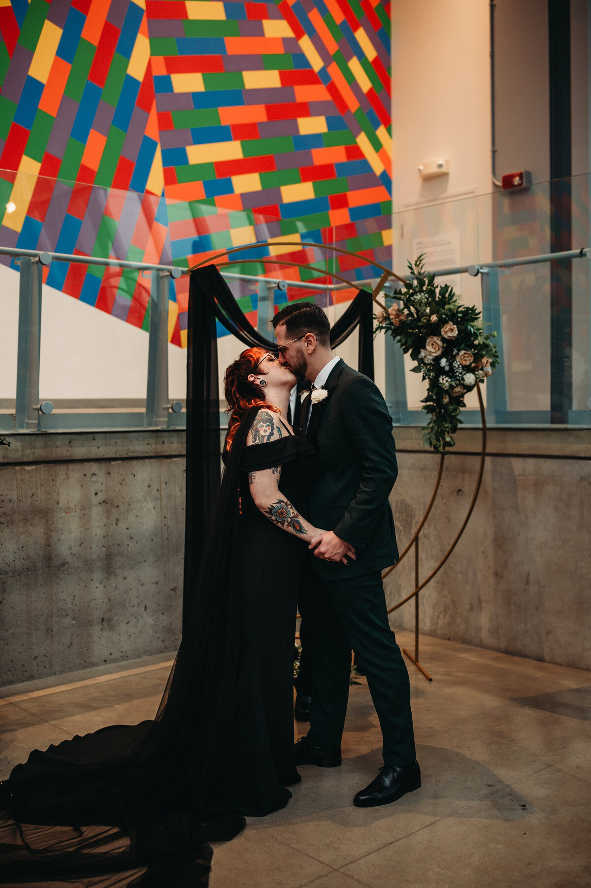 Alternative couple complete their frist kiss in front of a modern arch in Fall ceremony.