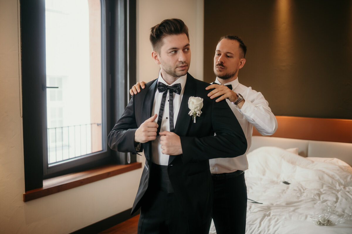 The best man helps the groom adjusting his jacket during getting ready session.