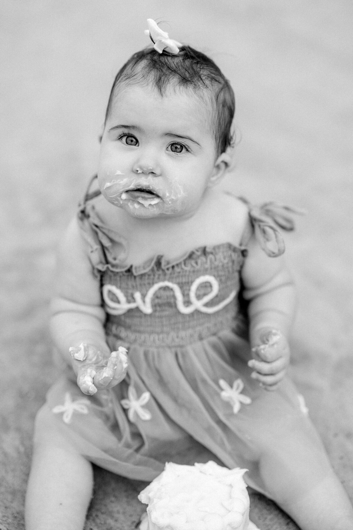 One-year-old baby girl with cake on face, fun first birthday portrait in Wilmington