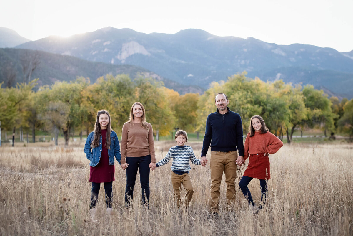 An image captured by a Colorado Springs family photographer of a family of 5 holding hands while standing in a field at sunset