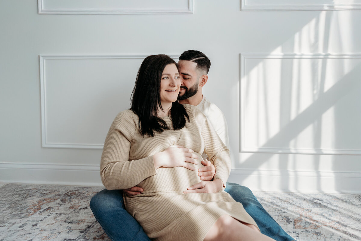 dad whispering to his wifes ear as they await the birth of their son during a studio photoshoot in Bartlett, IL