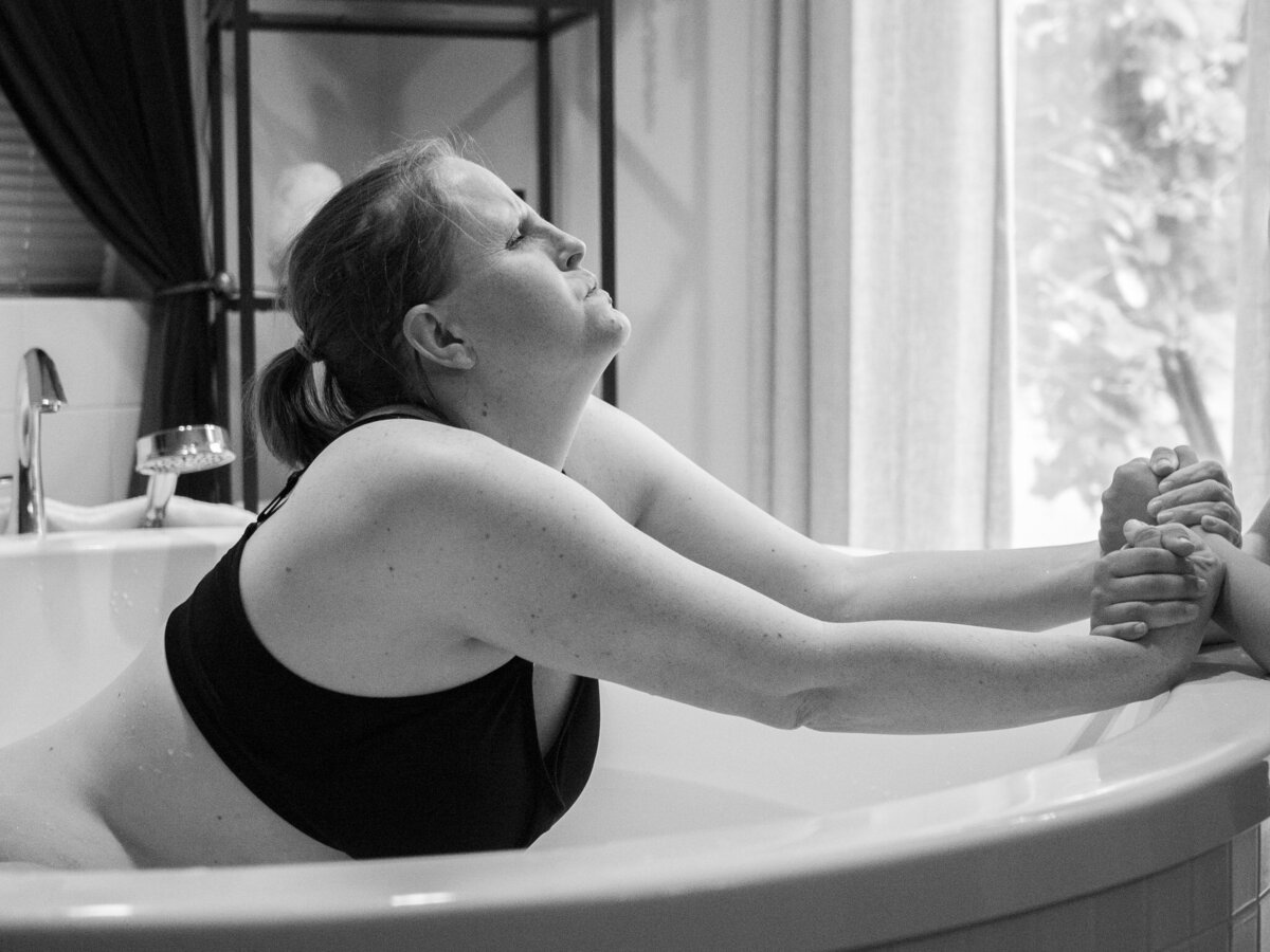 a woman labors in a birthing tub and is holding her support persons hands as she endures a contraction.