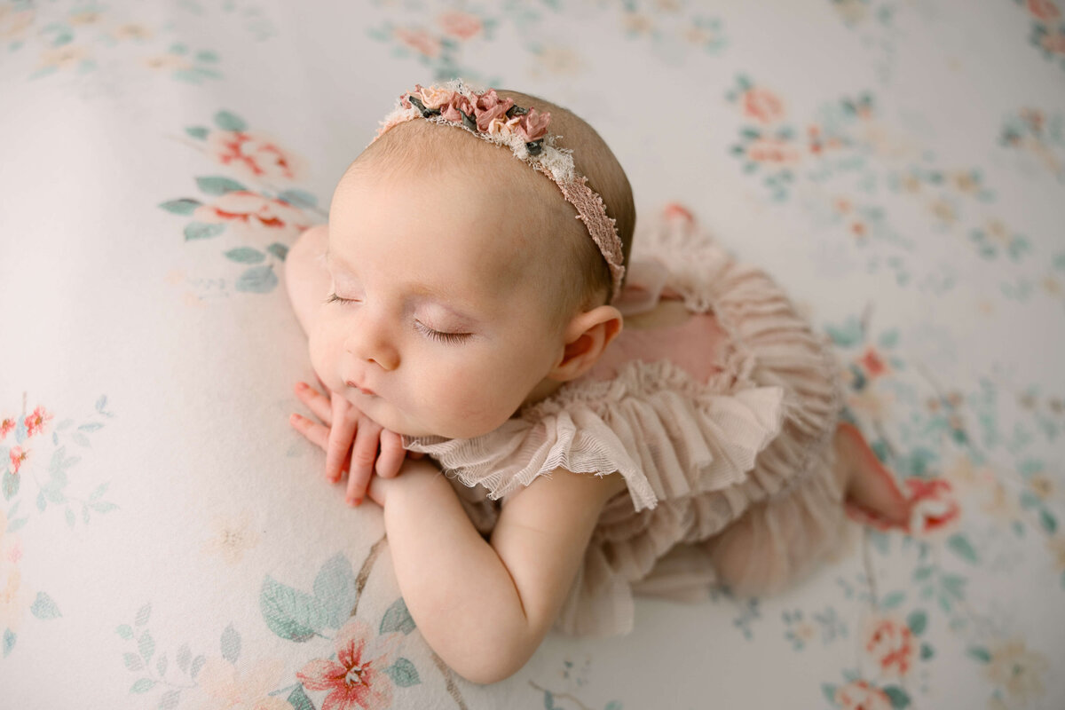 Sweet little newborn baby girl laying chin on hands on a flower backdrop