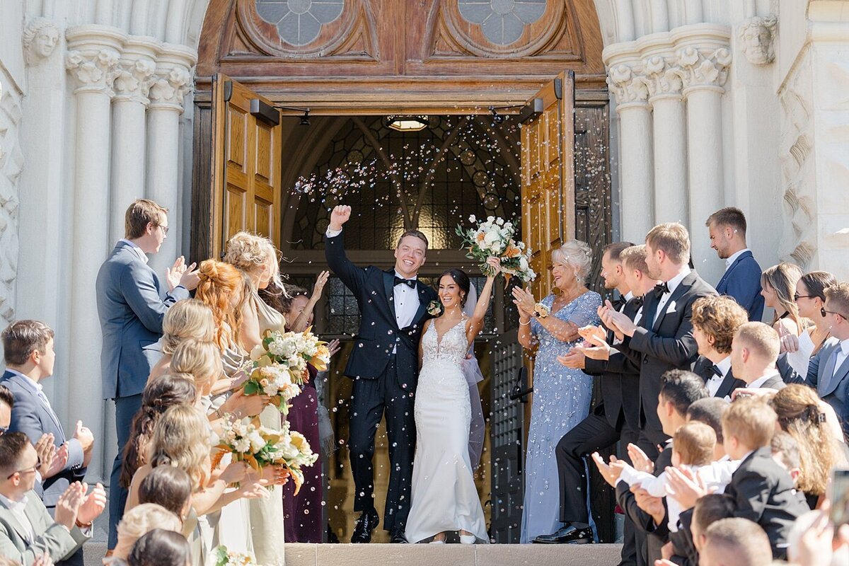 Columbus wedding  photographer  photographs bride adn groom exiting a cathedral while their guests throw rice at them in celebration and cheer for them