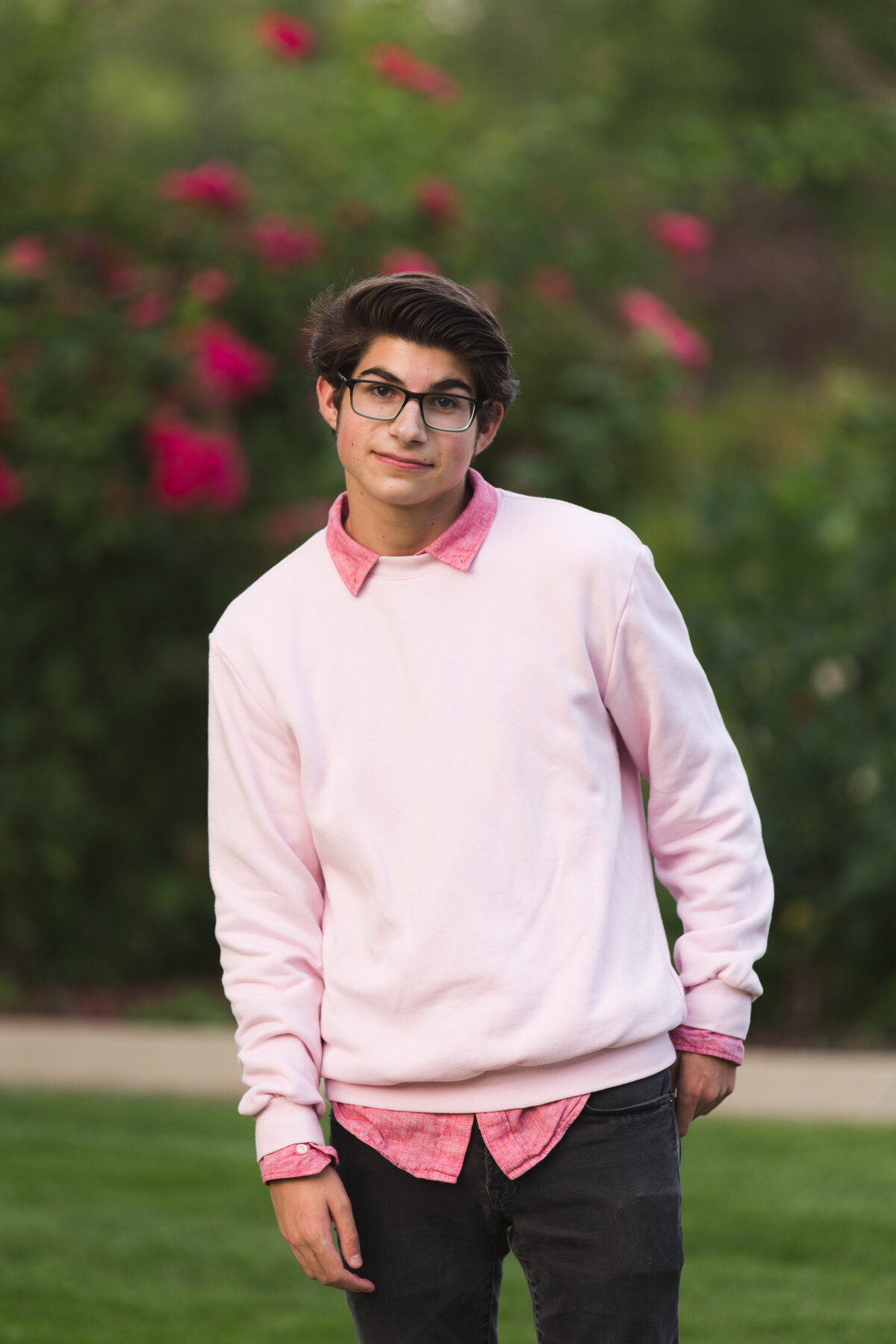 a high school senior in  a pink sweater stands by roses