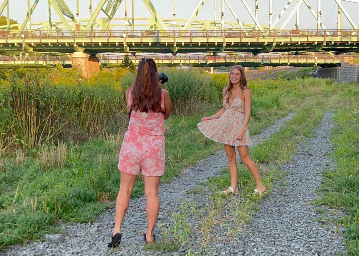 Photographer taking Senior portraits in front of flowers and a bridge