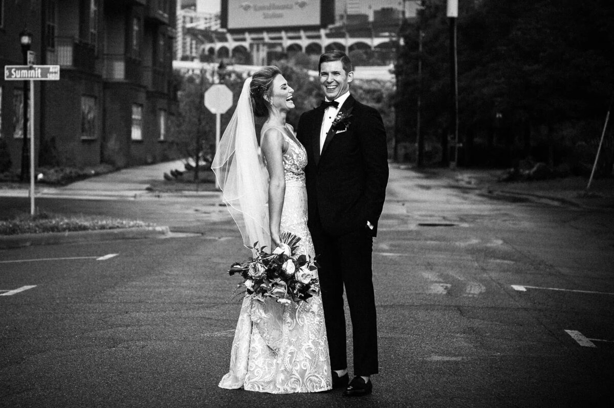 A bride and groom smiling while standing in the middle of the road.