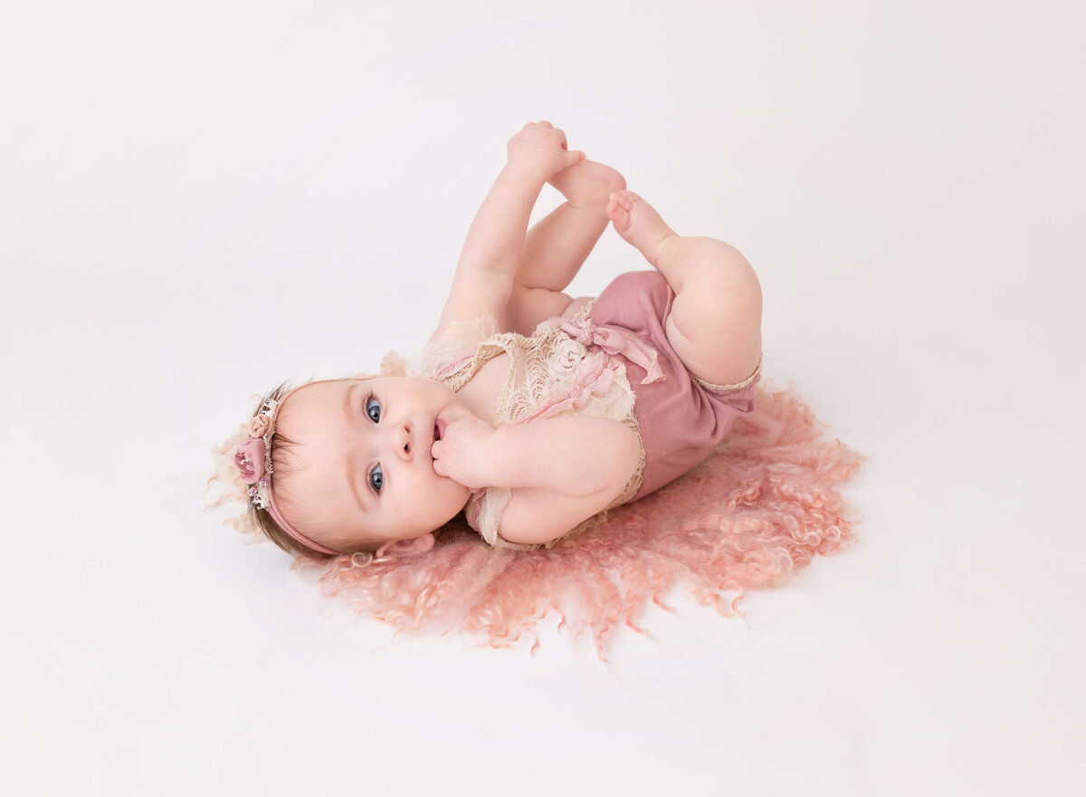 7-month-old baby girl in a mauve outfit holding her feet and smiling for her milestone session by a NYC baby photographer