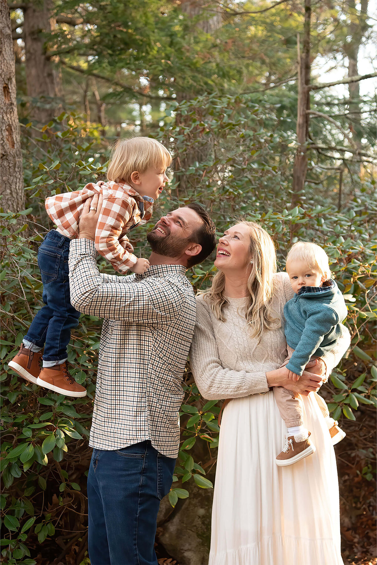 A dad holds up his toddler in the air while the mom looks on with their youngest on her hip at Whip Hill Park.