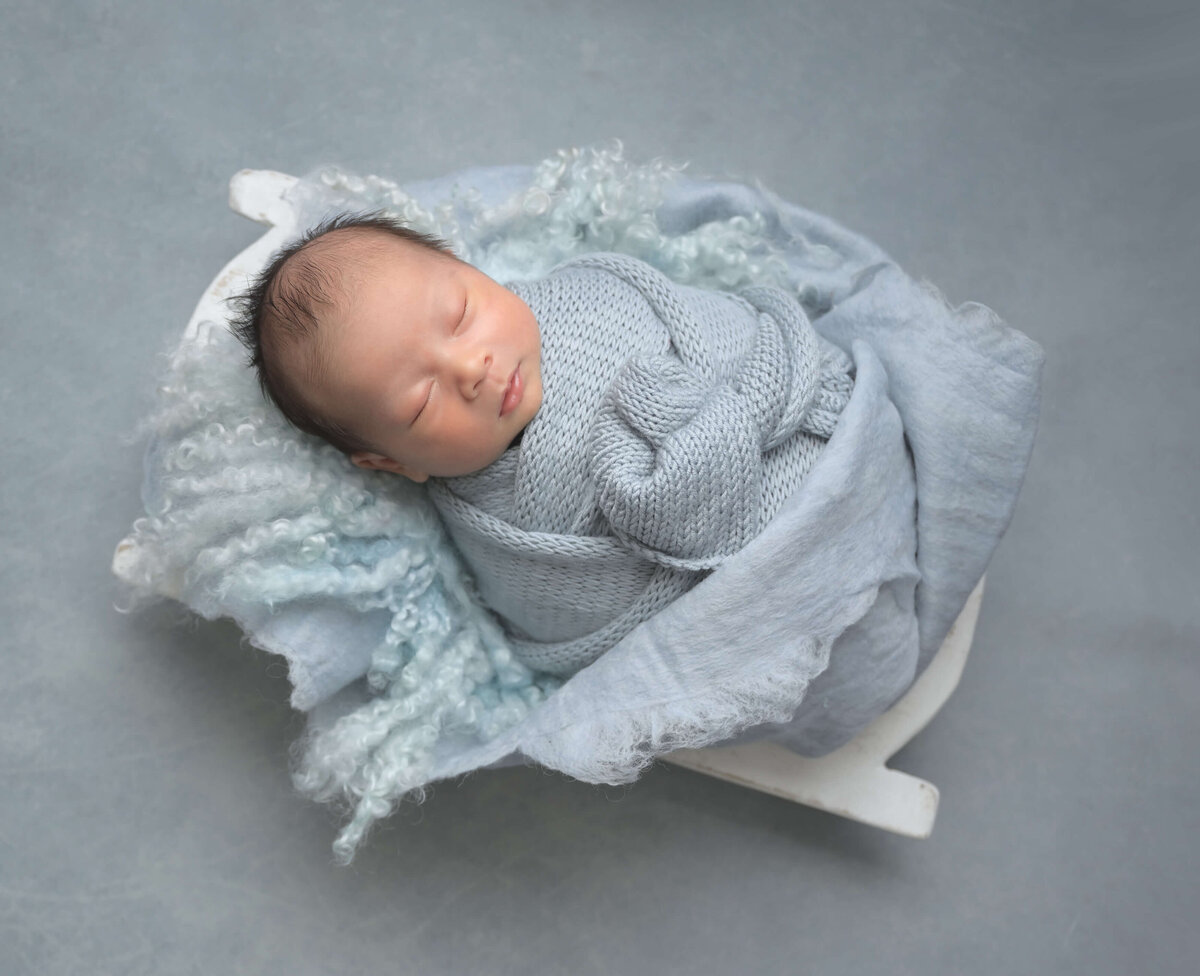 Studio-like newborn session of baby sleeping while snugly wrapped in light blue wraps.
