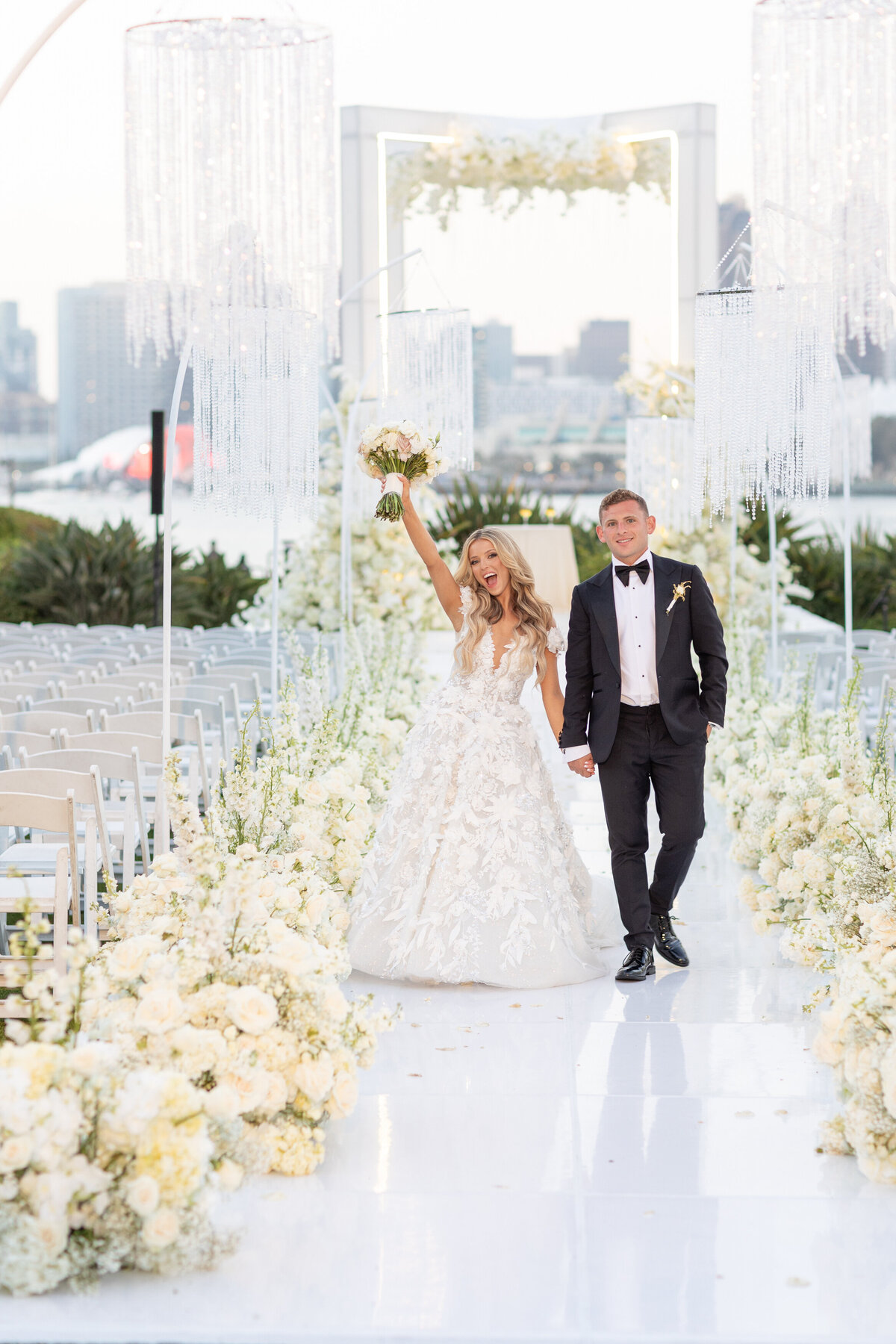 A bride and groom walking up a aisle as she holds up a bouquet of flowers