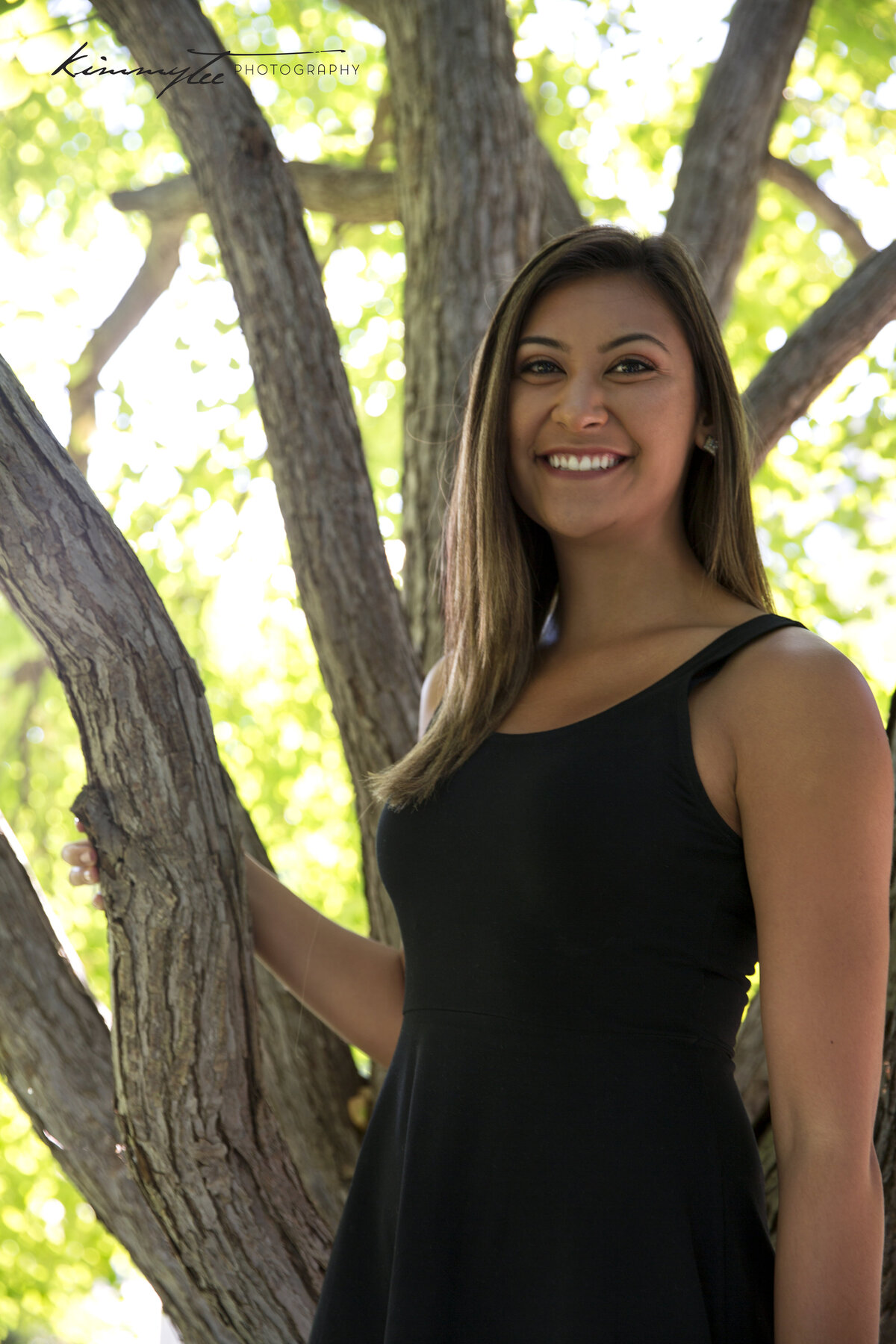 Smiling girl in black dress holding onto tree