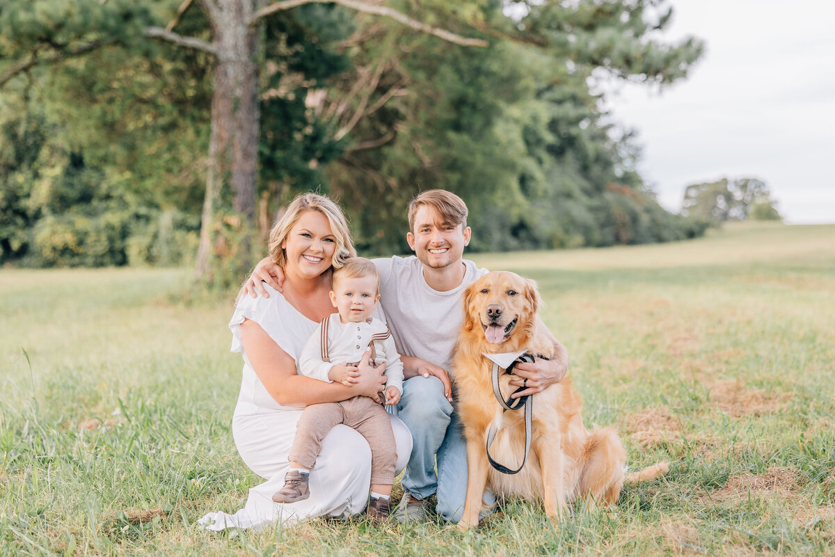 couple with baby and dog sitting in the grass