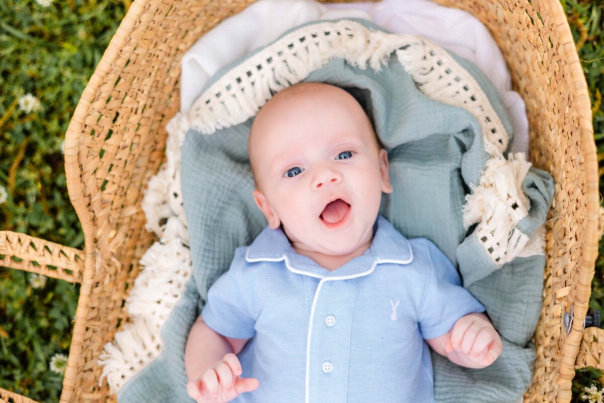 baby boy wearing a blue and white outfit laying in a moses basket smiling